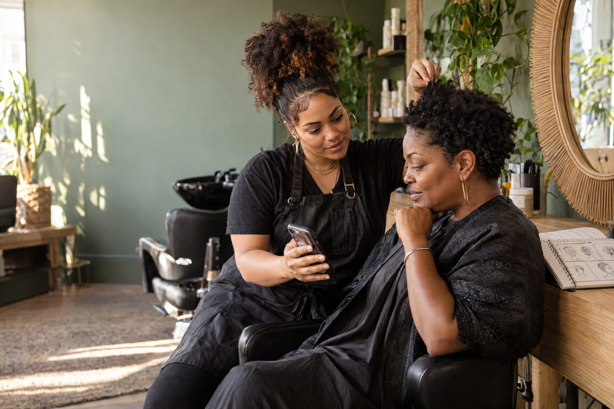 A stylist and a new client looking at inspiration photos on a phone together during a consult.